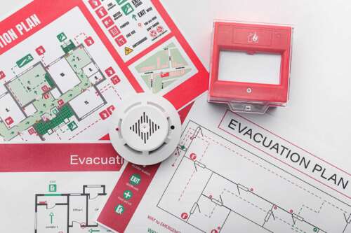 Set of fire safety evacuation plans with a fire alarm sitting on top of them