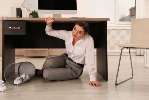 woman hiding under her desk during an active shooter situation in the workplace